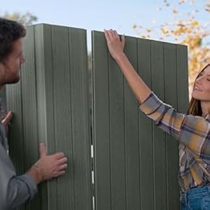 Deux personnes peignent une clôture ou un portail extérieur en bois de couleur vert sauge, montrant une activité collaborative d'entretien de la maison.