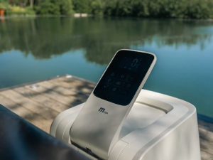 Appareil électronique placé sur une surface blanche près d'un quai ou d'une jetée au bord de l'eau, avec un lac et des arbres visibles en arrière-plan.