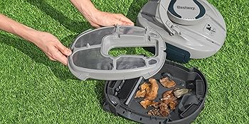 Démonstration d'un distributeur de friandises en plastique gris ouvert, rempli de friandises pour chiens et distribué sur de l'herbe.