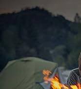 une femme assise à côté d'un feu de camp à côté d'une tente