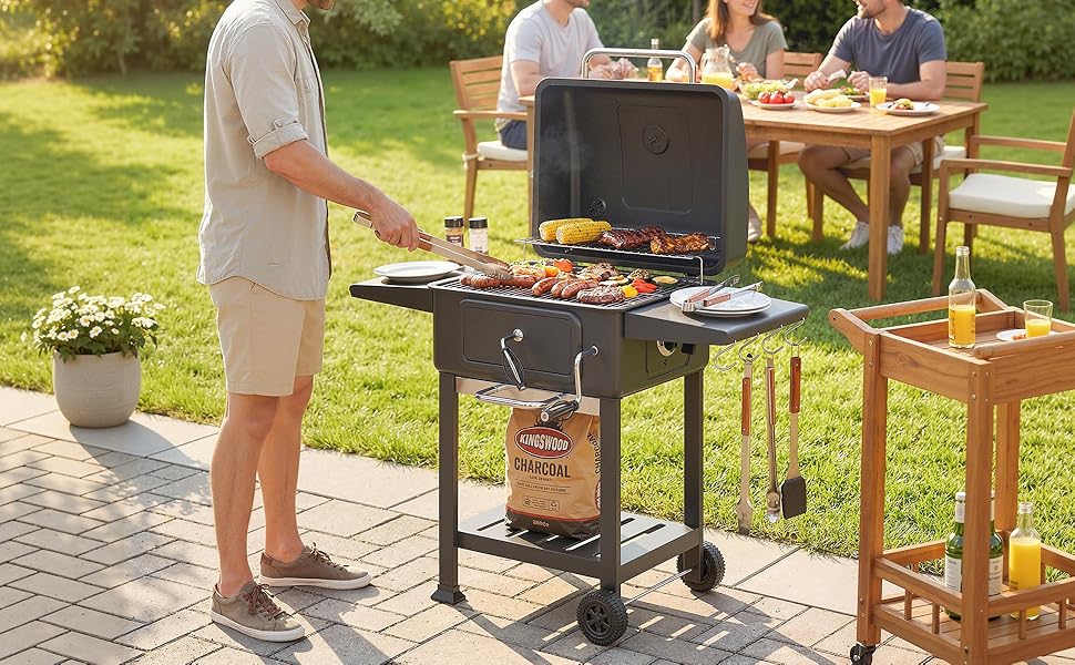 Scène de barbecue en plein air avec un grand barbecue au charbon de bois noir sur la terrasse, avec des aliments cuits sur des grilles. Table en bois et personnes se rassemblant dans un jardin ensoleillé.