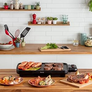 Scène de comptoir de cuisine avec grill électrique cuisant diverses viandes, ainsi que des plats préparés sur une planche à découper en bois. Fond de mur en brique blanche avec étagère affichant des articles de cuisine.