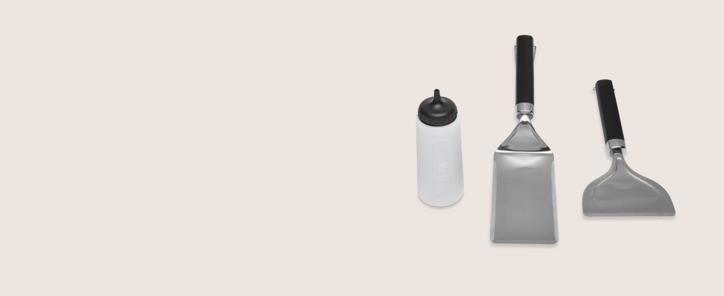 Ensemble de trois outils de nettoyage ou de grattage en acier inoxydable avec poignées noires sur fond beige.
