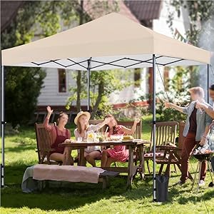 Grande tente à baldaquin beige au-dessus de la salle à manger extérieure. Des gens assis à une table en bois avec des chaises, savourant un repas dans le jardin.