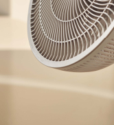 Gros plan d'une pale de ventilateur électrique blanche, montrant des aubes en plastique incurvées sur fond beige. Le ventilateur semble être en mouvement, ce qui crée un effet de spirale.