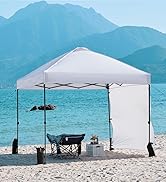 Tente à baldaquin escamotable blanche sur une plage, fournissant de l'ombre pour les chaises et une table. Montagnes et eau turquoise visibles en arrière-plan.