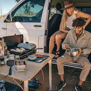 Personnes représentées assises et se prélassant dans ce qui semble être un site de camping ou de loisirs en plein air à proximité de véhicules, ce qui suggère un contexte d'utilisation mobile ou portable.