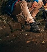 Personne portant des chaussures et des pantalons de randonnée, assise à l'extérieur sur un sol rocheux près d'un feu de camp. Concentrez-vous sur les chaussures et le bas des jambes.