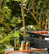Grill extérieur avec cuisson de saucisses, accompagné d'une bouteille en verre vert et de bouteilles de condiments sur une surface en bois. Feuillage vert feuillu en arrière-plan.