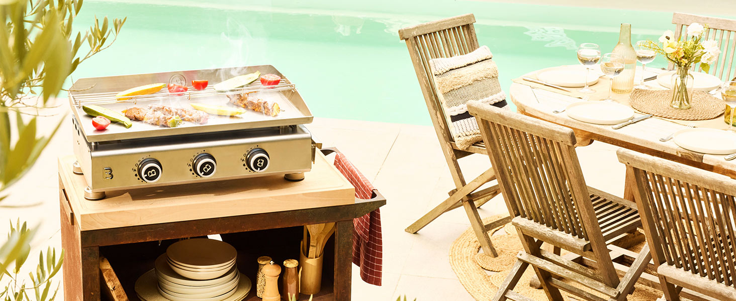 Mobilier d'extérieur en bois comprenant un coffre de rangement tissé avec fermoirs en métal, une chaise en bois à dossier en échelle et une table sur un patio ensoleillé avec des éléments décoratifs tissés et un éclairage naturel.