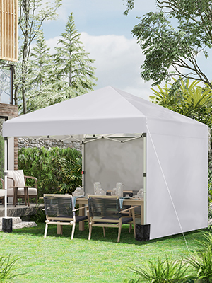 Image 1 : Tente à baldaquin escamotable blanche avec parois latérales installée dans un jardin extérieur. Meubles en bois visibles à l'intérieur, entourés d'un aménagement paysager verdoyant et d'arbres.