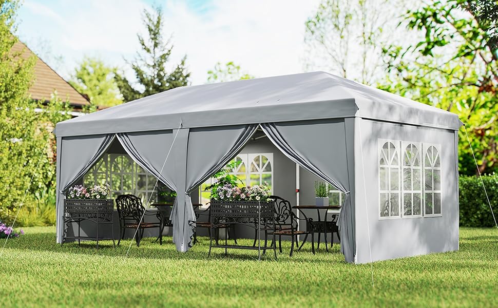 avec murs et toit en tissu gris. Comprend des panneaux latéraux avec fenêtres et rideaux. Installé sur la pelouse avec des meubles de patio visibles à l'intérieur.