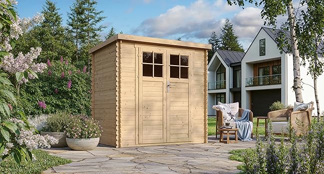 Abri de jardin en bois avec portes et fenêtres doubles, placé sur un patio en pierre. Maison moderne et jardin paysager visibles en arrière-plan.
