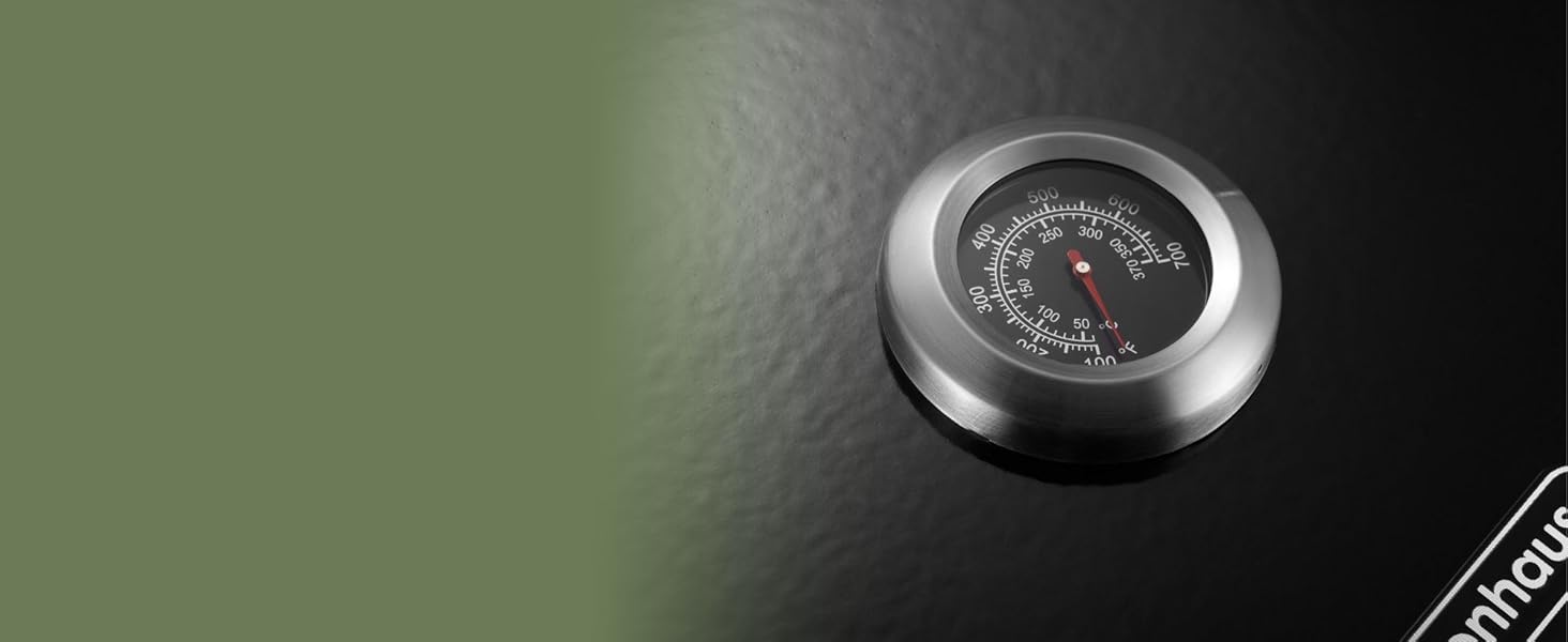 Gros plan d'un thermomètre ou d'une jauge de température rond en argent avec une face noire et une aiguille indicatrice rouge. Partiellement visible sur fond vert.