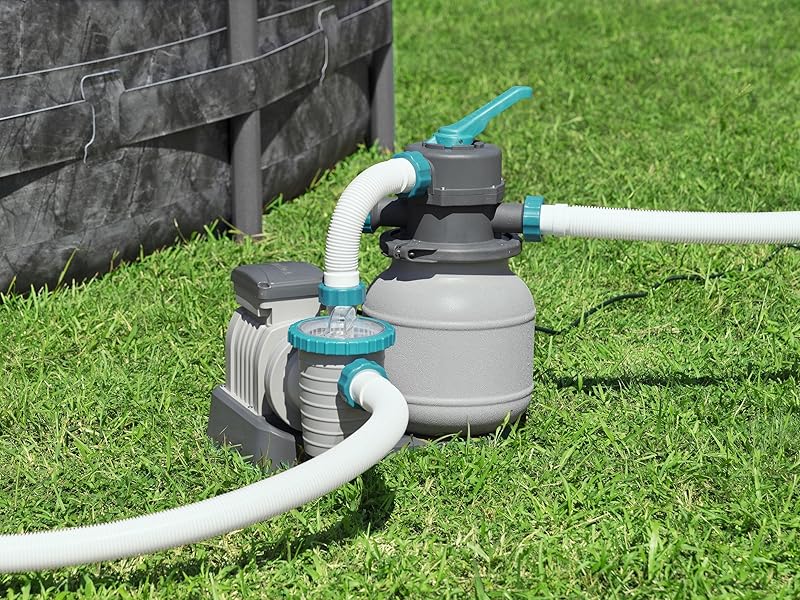 avec raccords bleus et tuyaux en PVC blanc installés sur du gazon près d'un mur de soutènement.