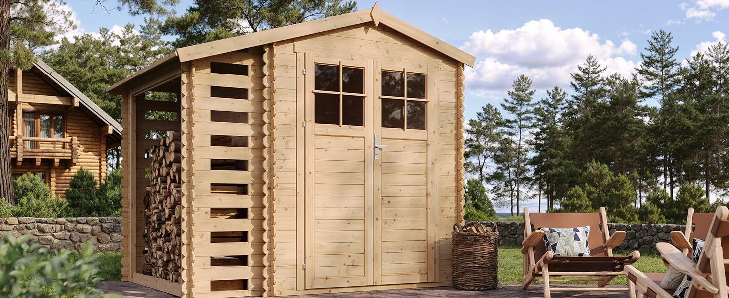 avec support de rangement pour bois de chauffage attaché. La structure présente un toit en pointe, des portes doubles avec fenêtres et est située sur un patio en pierre dans un cadre de pinède