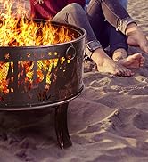 Gros plan des pieds près d'un foyer métallique avec des flammes sur une plage de sable, créant une atmosphère extérieure chaleureuse