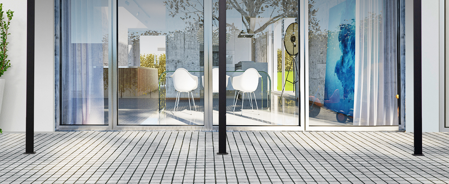 Intérieur moderne avec portes coulissantes en verre ouvrant sur un patio. Des chaises et des tables blanches sont visibles à l'intérieur, avec des plantes et des sols extérieurs à l'extérieur.