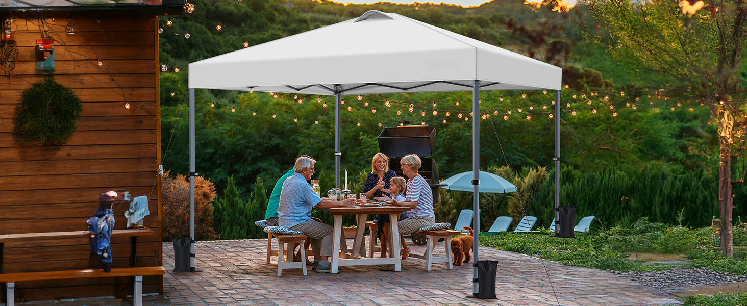 au-dessus de la salle à manger extérieure. Groupe assis à une table en bois. Guirlandes lumineuses et meubles de patio visibles. Cadre arrière avec verdure et structure en bois.