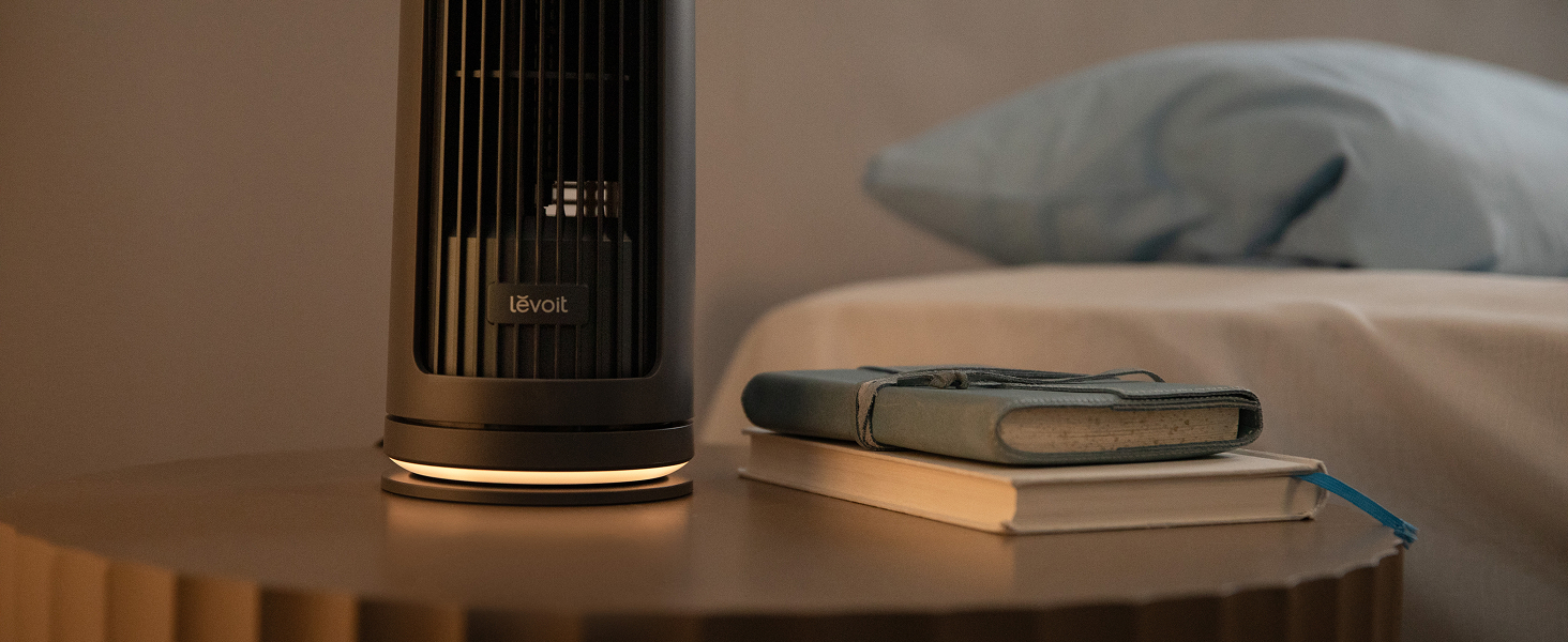 Haut-parleur intelligent cylindrique noir sur une surface en bois à côté d'un pavé de commande rond, positionné sur une table dans l'aménagement intérieur de la maison.