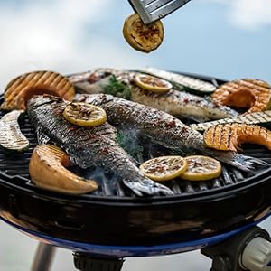 Grille à griller circulaire avec poisson entier, tranches de citron et légumes à cuire. Pinces qui ajoutent une tranche de citron aux plats grillés