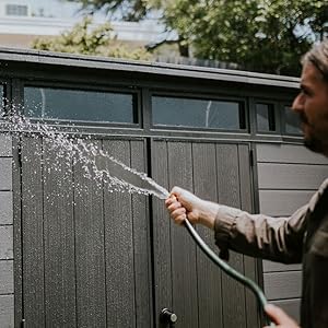 Démonstration de lavage à pression ou de pulvérisation d'une clôture sombre à l'extérieur, montrant un motif de pulvérisation d'eau contre la surface de la clôture.