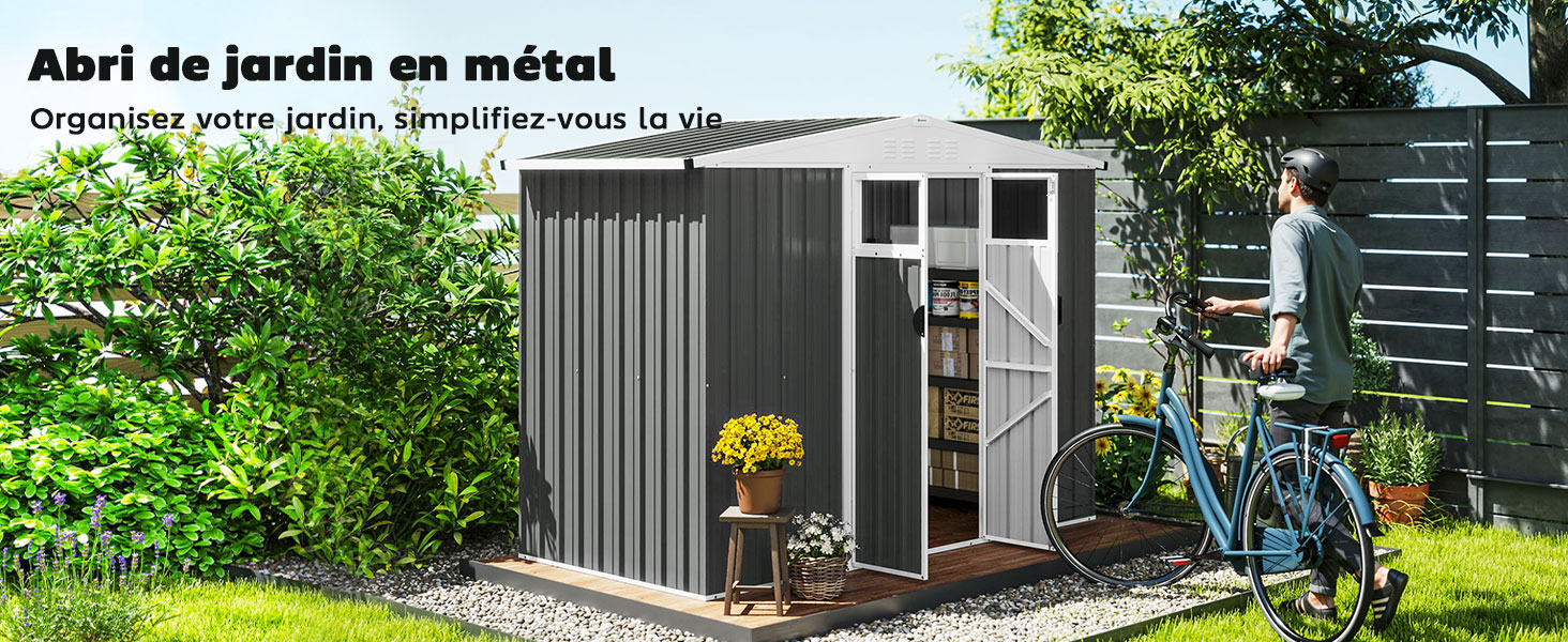 en métal gris avec portes blanches dans un décor de jardin. Doté de murs ondulés et d'un toit en pente, il est entouré de verdure. Un vélo bleu est adossé à une clôture en bois située à proximité