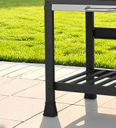 Gros plan d'un pied de meuble d'extérieur en métal noir sur des carreaux de patio beiges, avec de l'herbe verte en arrière-plan. Le cadre a une étagère inférieure à lattes et une barre supérieure argentée visible.