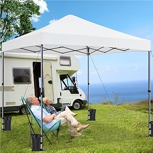 Tente à baldaquin blanc installée à côté du camping-car. Personne se relaxant dans une chaise pliante sous la tente, avec vue panoramique sur la côte.