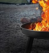 avec des flammes intenses brûlant dans un bol en métal sur trois pieds. Le pied d'une personne dans une chaussure brune visible près du bord.