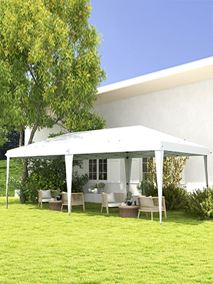 Grande tente extérieure blanche à baldaquin installée sur une pelouse à côté d'une maison. Meubles de patio visibles en dessous.
