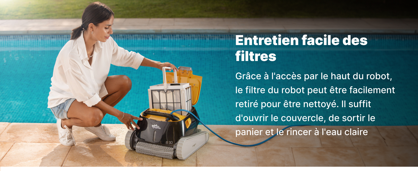 Femme en robe blanche agenouillée au bord de la piscine, tendant la main dans un robot nettoyeur de piscine jaune. Le texte décrit la maintenance facile des filtres grâce à un accès par le haut.