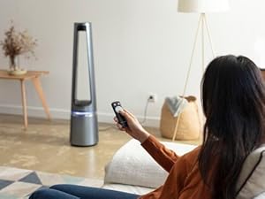 Une femme sur son canapé allumant son ventilateur purificateur eclipse à l'aide de sa télécommande