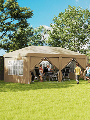 Grande tente extérieure beige à baldaquin avec fenêtres en filet installées sur l'herbe. Les personnes visibles à l'intérieur l'utilisent comme espace de rassemblement ombragé avec des chaises.