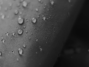 Gros plan de gouttelettes d'eau perlant sur la surface d'un tissu imperméable texturé foncé, démontrant