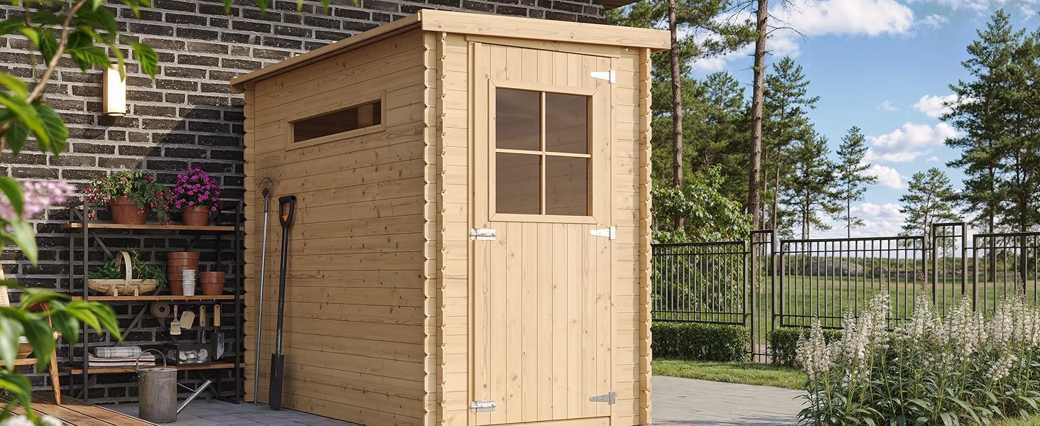 Petit abri de jardin en bois avec toit en pente et fenêtre unique, placé sur un patio près d'un mur de briques. Entouré de plantes et de mobilier d'extérieur dans le jardin.