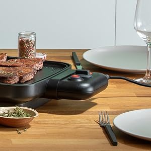 Set de table avec poêle noire, assiettes vides, couverts et verre à vin sur une surface en bois.
