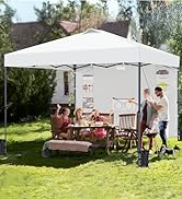 Grande tente à baldaquin escamotable blanche installée dans le jardin. La famille s'est réunie en dessous pour un repas en plein air. Meubles en bois, barbecue visible. La tente fournit de l'ombre pour les repas et les activités de cuisine.