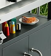 Armoire de rangement gris foncé avec poignées en métal, présentant des bouteilles de condiments et une assiette de crevettes sur une étagère sur fond de feuillage vert
