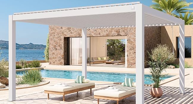 Panorama de la propriété de luxe en bord de mer montrant une structure de pergola blanche, une piscine et une vue sur l'océan avec une architecture en pierre moderne et un aménagement paysager.