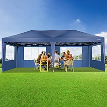 Grande tente extérieure bleue installée sur de l'herbe verte. Personnes visibles à l'intérieur, suggérant une utilisation pour des rassemblements ou des événements.